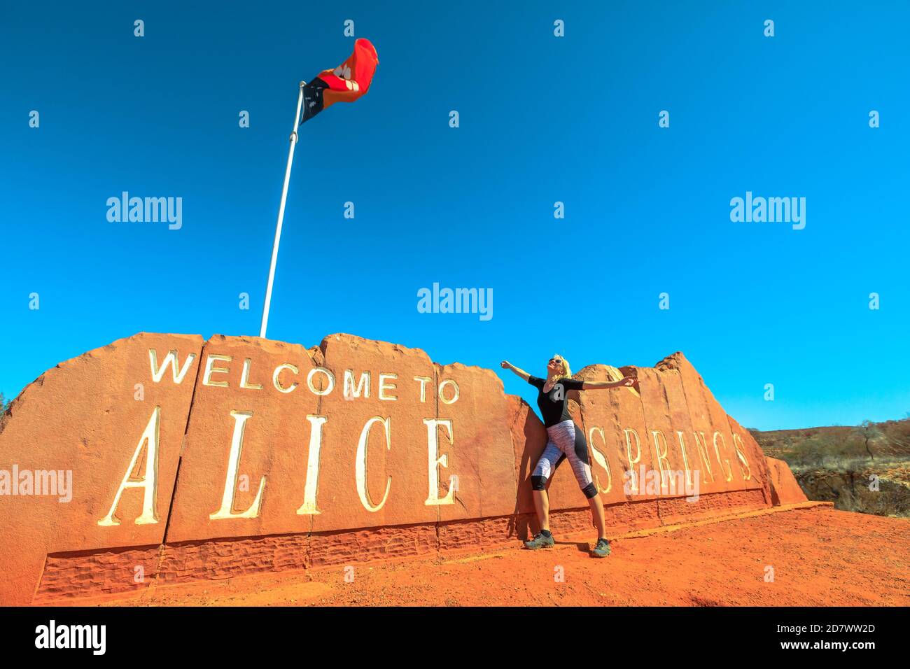 Happy Carefree Tourist Woman in Alice Springs Welcome Sign in Central Australia. Tourismus im Outback Red Centre Wüste. Reise Entdeckung Roadtrip in Stockfoto