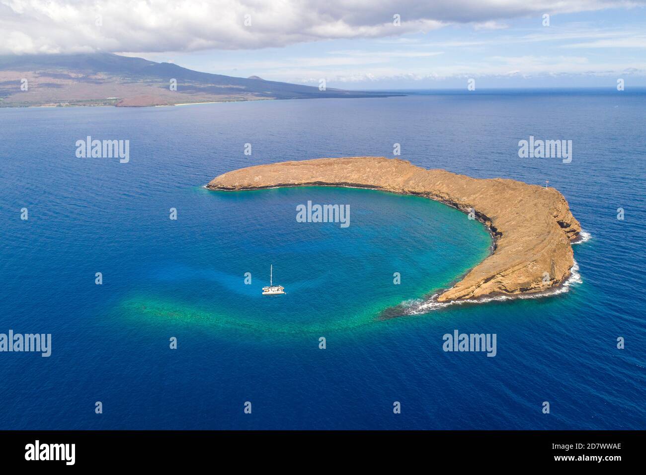 Molokini Krater, Luftaufnahme der gesamten halbmondförmigen Insel mit einem Charterboot und der Insel Maui im Hintergrund, Hawaii. Stockfoto
