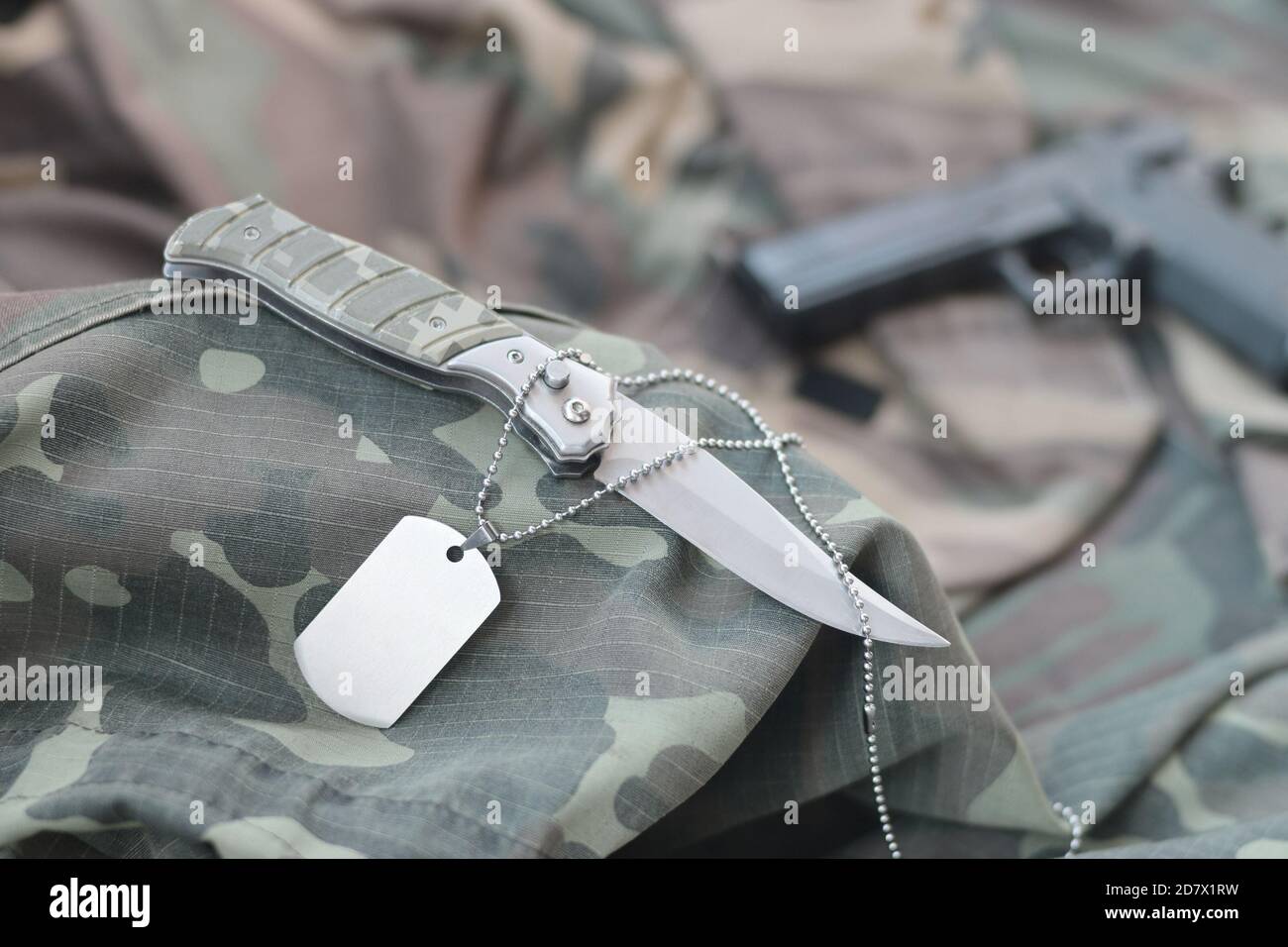 Arme-Hund-Tag-Token mit Messer und Pistole liegen auf gefaltetem, tarngrünen Stoff. Ein Set von Militärveteranen oder Trophäen-Kit für alte Aufgaben Stockfoto