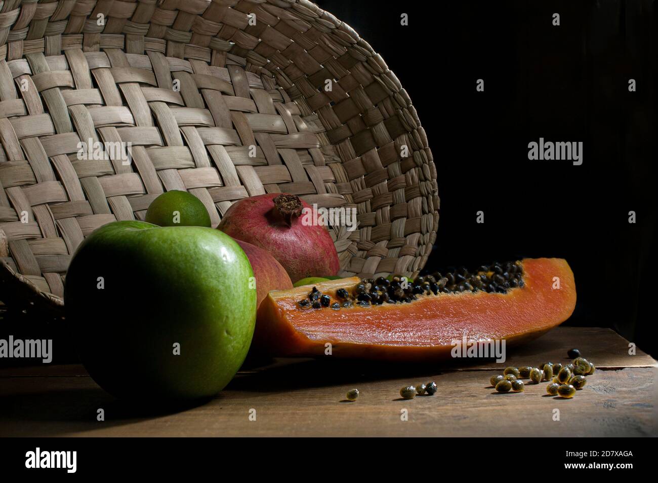 Stillleben, Papaya Scheibe mit Samen auf der Oberseite, Granatapfel, Pfirsich, grüner Apfel und Zitrone auf einem rustikalen Holztisch mit einem handgemachten Korb. Chiaroscuro Stockfoto
