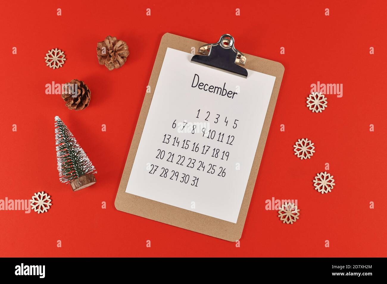 Weihnachts-Wohnung lag mit Zwischenablage mit Kalenderblatt für den Monat Dezember umgeben von kleinen Weihnachtsbäumen, Pinienzapfen, Schneebällen und Schneeflocken Stockfoto