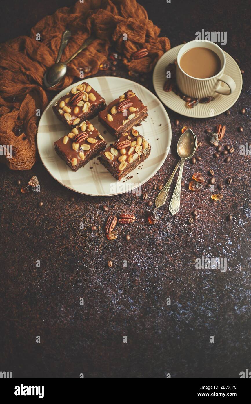 Die quadratischen Stücke von leckeren Karamellkuchen mit Erdnüssen und paranüsse mit Milchkaffee serviert Stockfoto
