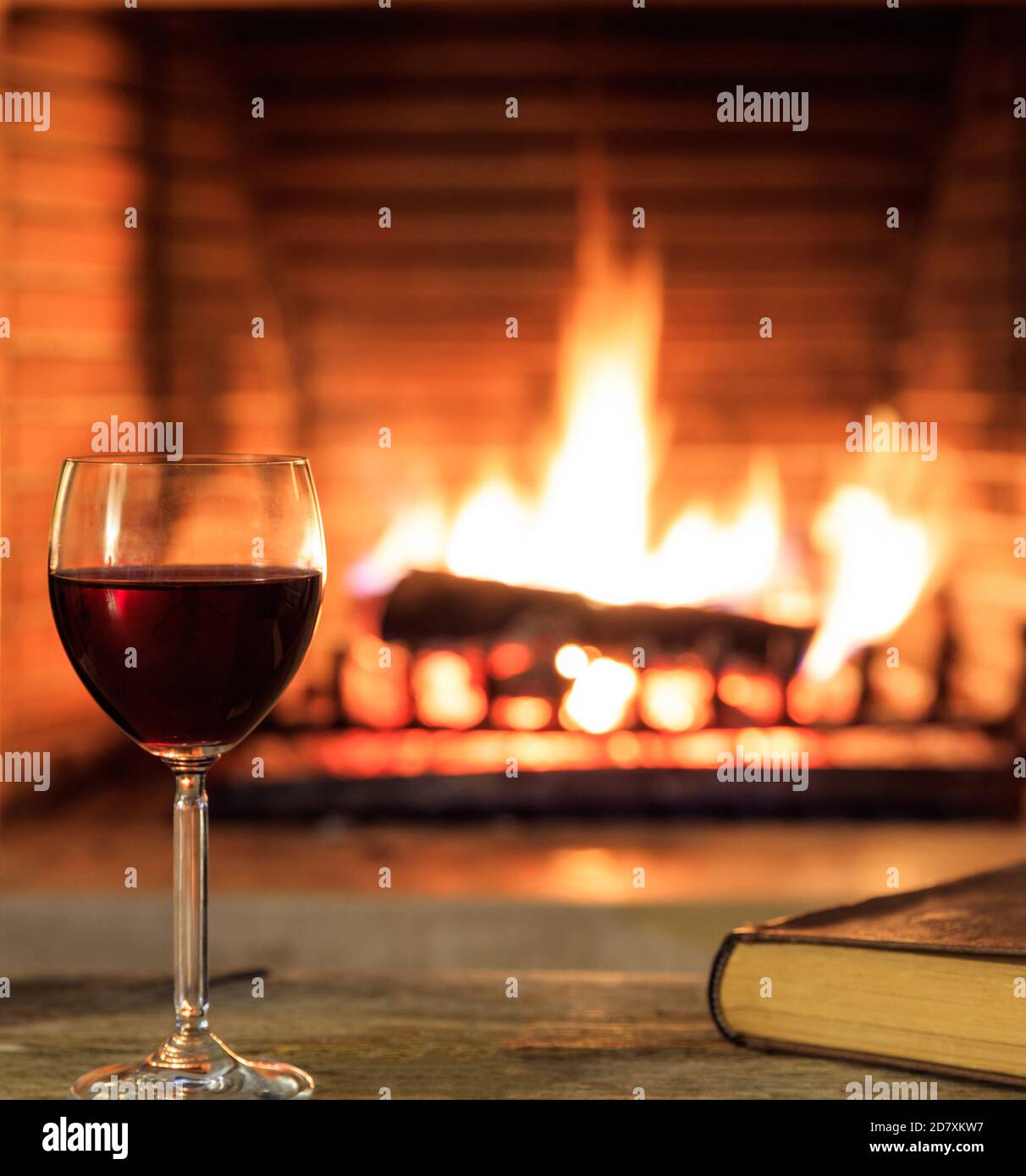 Ein Glas Rotwein und ein Buch über brennenden Kamin Hintergrund. Warme gemütliche Inneneinrichtung, Winterzeit Stockfoto