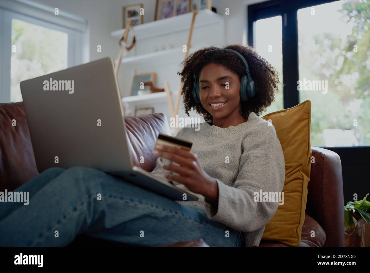 Fröhliche Frau, die Musik mit bluetooth-Kopfhörern online macht Transaktion mit EC-Karte und Laptop Stockfoto