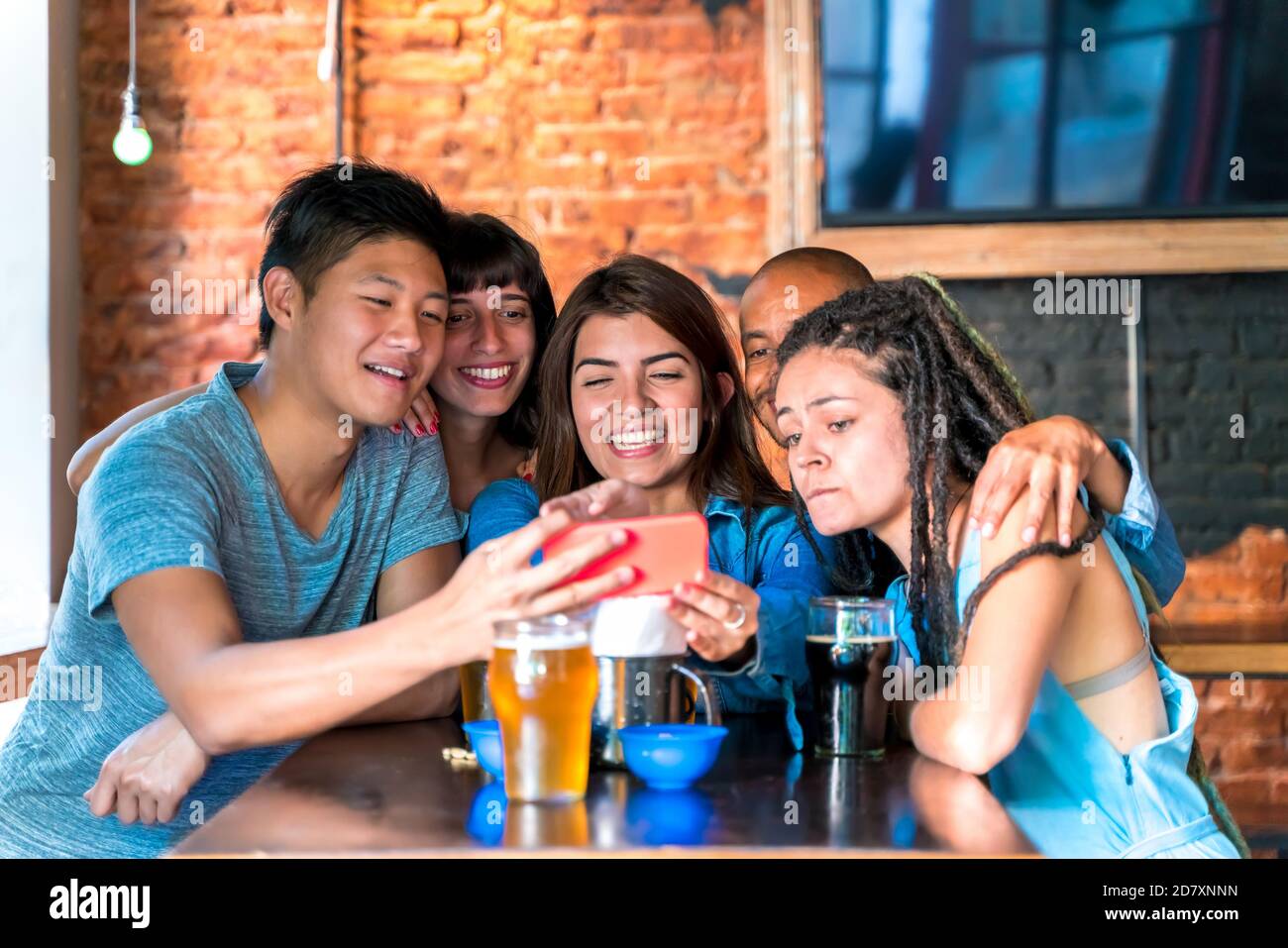 Eine Gruppe internationaler Freunde, die über Inhalte auf einem Smartphone-Bildschirm lachen. Stockfoto