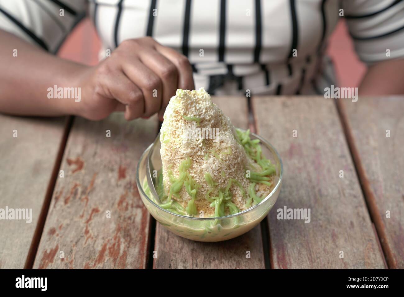 Frau Hand mit Löffel zu Cendol essen - ein süßes rasierte Eis mit grünem Reismehl Gelee Dessert. Stockfoto