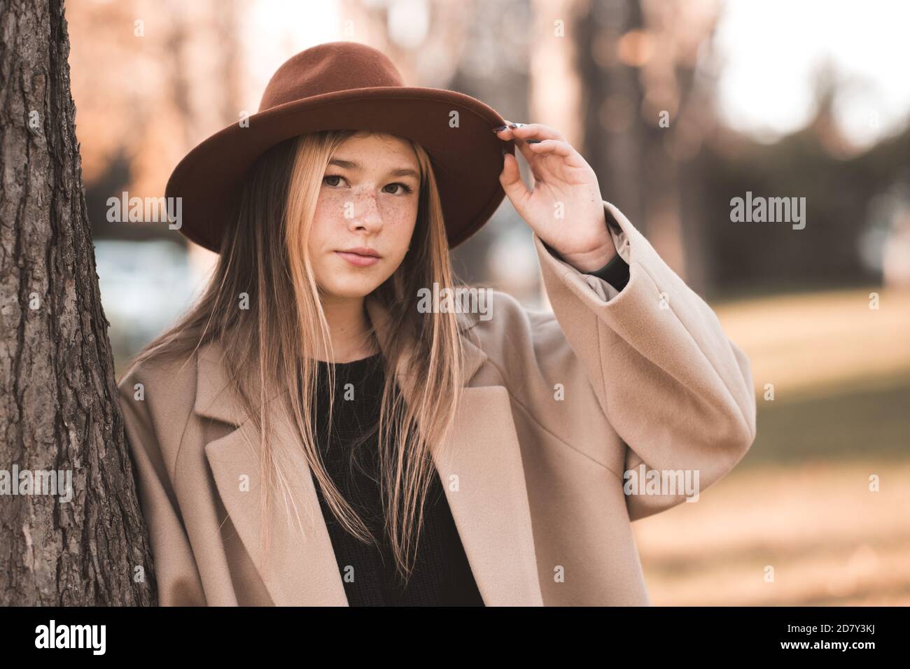 Lächelndes Teenager-Mädchen 13-14 Jahre alt trägt stilvolle Hut und beige Wintermantel posiert über Herbst Hintergrund Nahaufnahme. Teenagerhood. Stockfoto