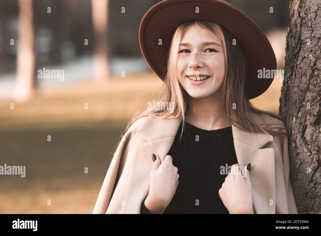 Lächelndes Teenager-Mädchen 13-14 Jahre alt trägt stilvolle Hut und beige Wintermantel posiert über Herbst Hintergrund Nahaufnahme. Teenagerhood. Stockfoto