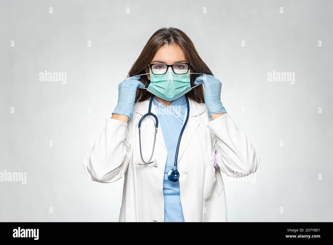 Selbstbewusste junge Ärztin in weißem Mantel, Latex-Schutzhandschuhe tragen medizinische Maske. Frau in medizinischen Handschuhen auf Schutzmaske. Coronavirus Stockfoto
