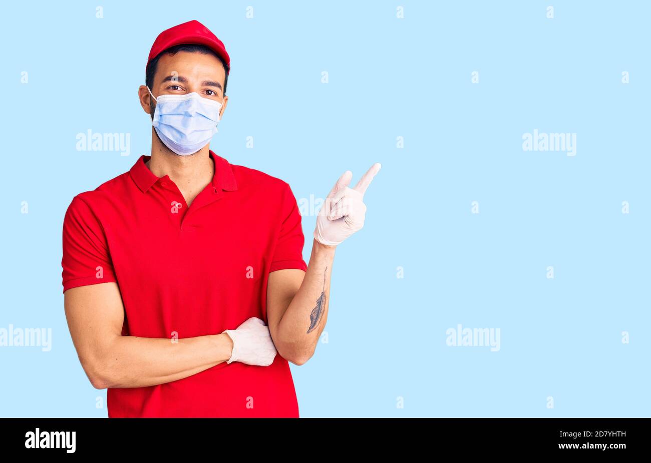 Junge gutaussehende hispanischen Mann trägt Lieferung Uniform und medizinische Maske Lächelnd glücklich zeigt mit Hand und Finger zur Seite Stockfoto