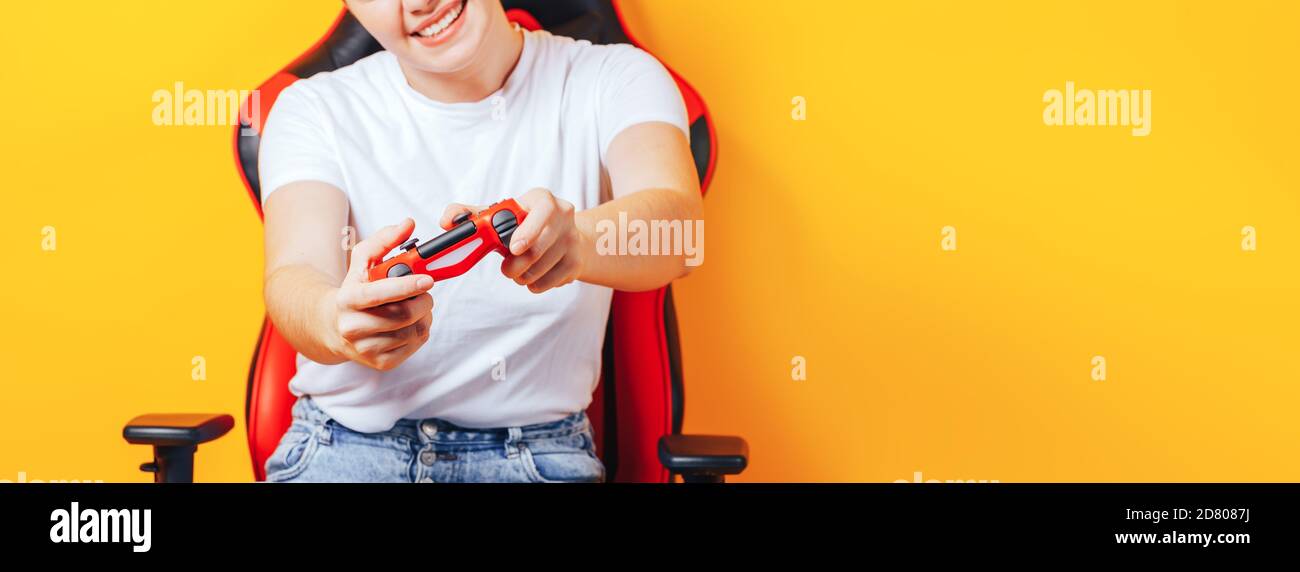 Frau, die hinter einem Spielstuhl in ihren Händen sitzt und rot hält Gamepad auf gelbem Hintergrund Stockfoto