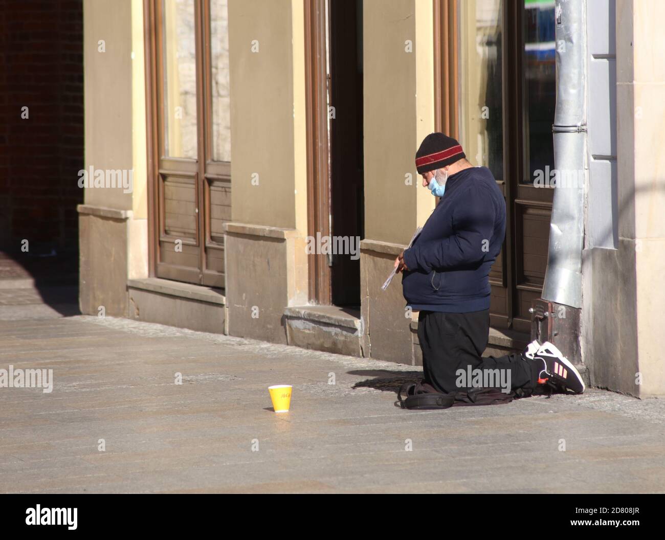 Krakau. Krakau. Polen. Maskierter Mann kniete auf dem Bürgersteig und bettelte um Geld. Stockfoto