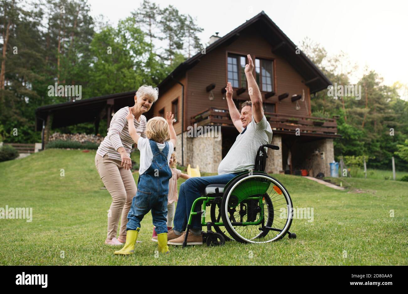 Kleine Kinder mit älteren Großeltern im Rollstuhl spielen. Stockfoto