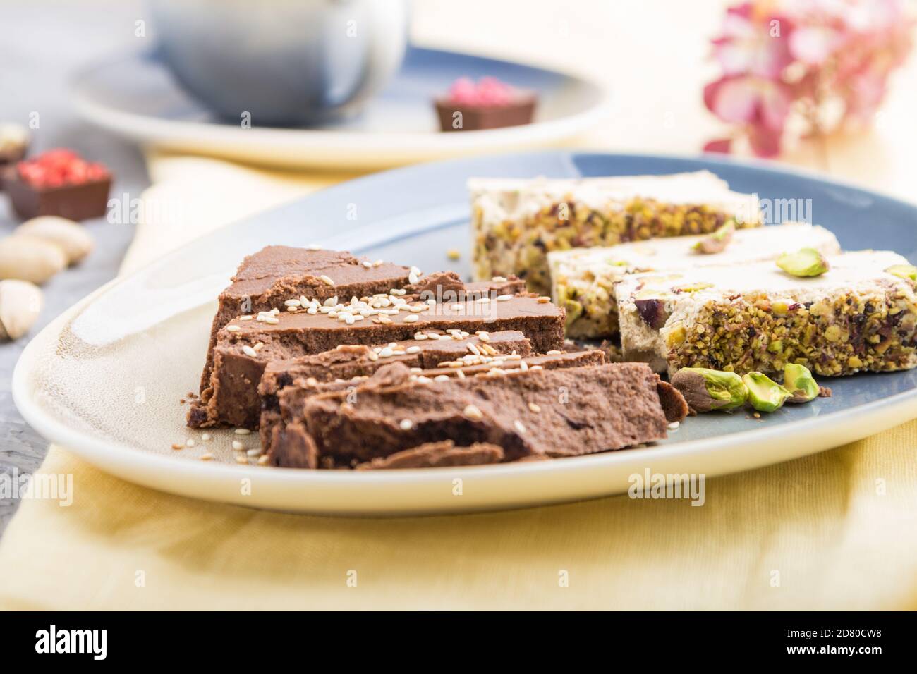Traditionelle arabische Süßigkeiten Sesam Halva mit Schokolade und Pistazie und eine Tasse Kaffee auf einem grauen Betongrund und gelben Textil. Seitenansicht, c Stockfoto