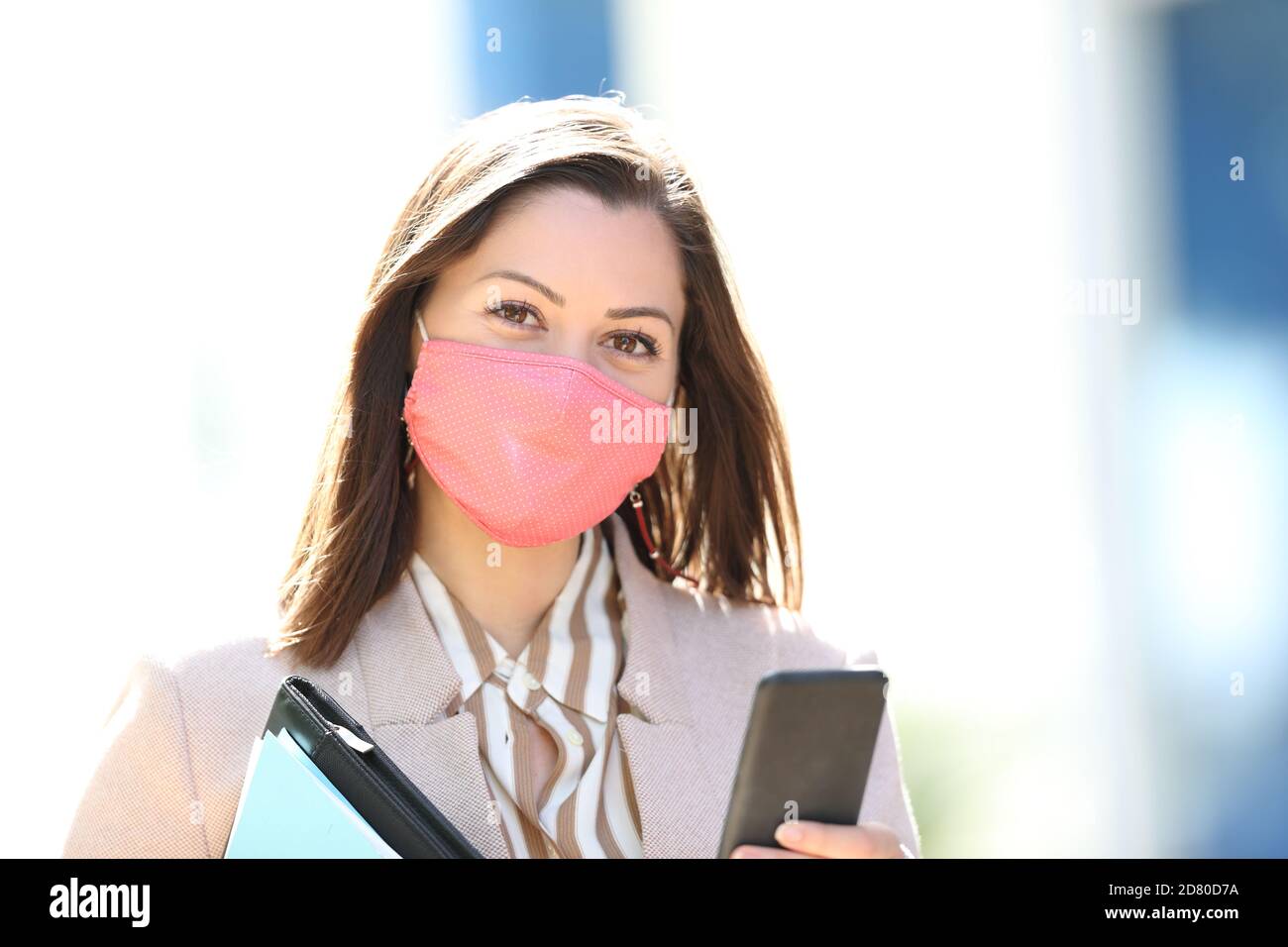 Happy Entrepreneur trägt Maske Vermeidung Coronavirus Ansteckung und hält smart Das Telefon posiert und sieht dich auf der Straße an Stockfoto