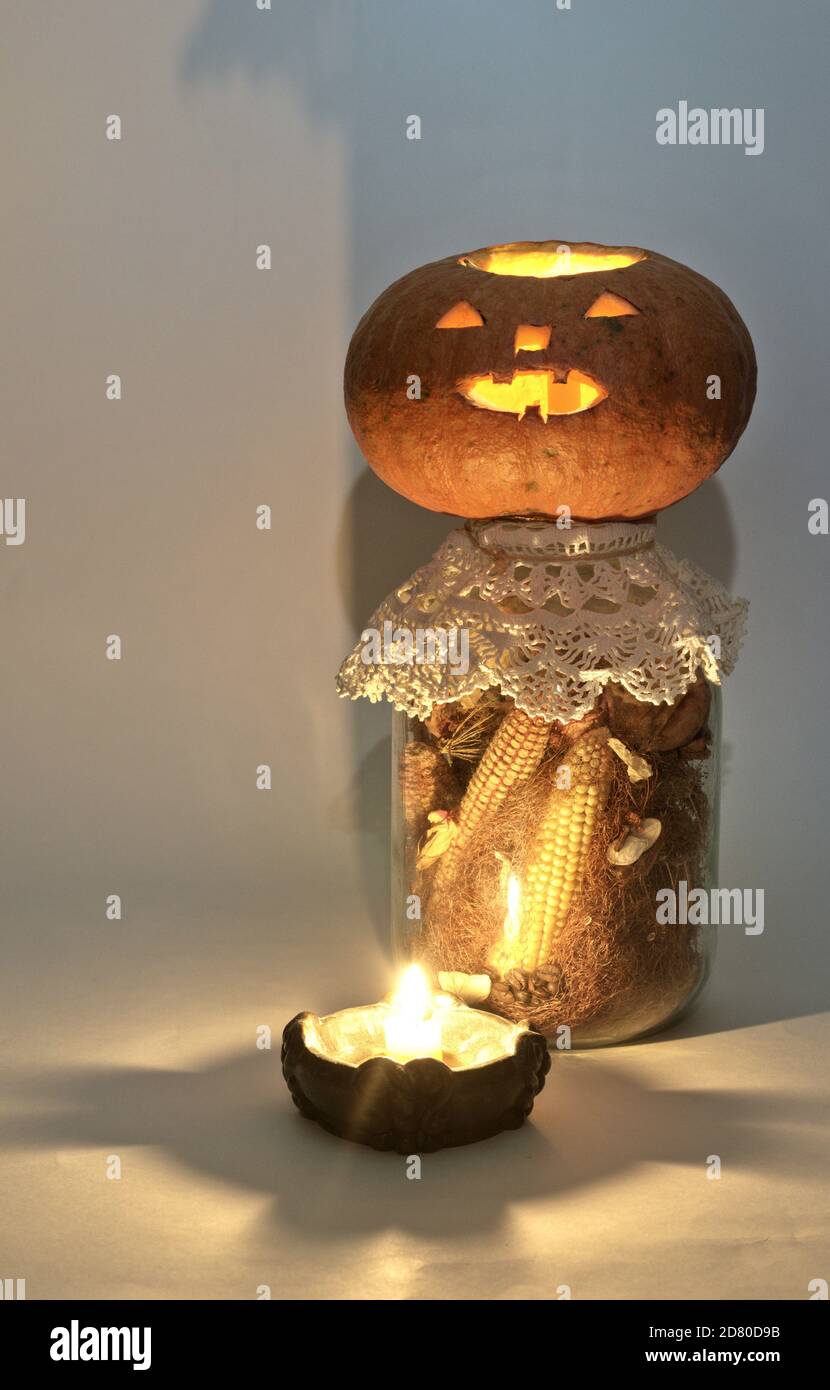 jack o Laterne auf großen Glas getrockneten Mais auf der Kohle und Maisseide. Am Kerzenhalter mit einer brennenden Kerze. Geheimnisvolle Schatten Stockfoto