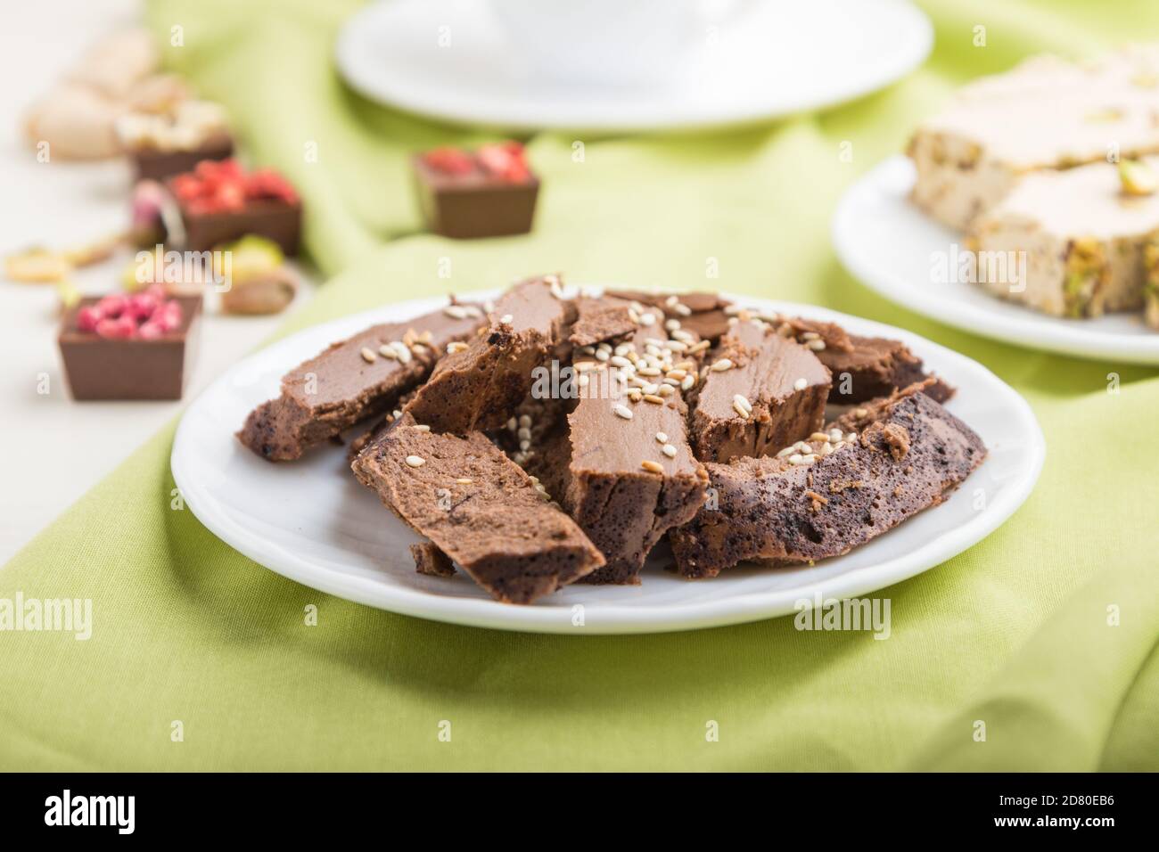 Traditionelle arabische Süßigkeiten Sesam Halva mit Schokolade und Pistazien und eine Tasse Kaffee auf grünem Textil-Hintergrund. Seitenansicht, Nahaufnahme, selektive fo Stockfoto