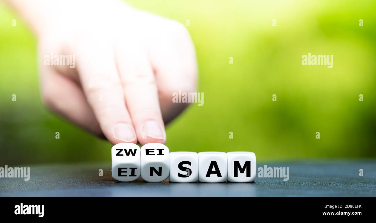 Hand dreht Würfel und ändert das deutsche Wort "einsam" in "zweierlei". Stockfoto