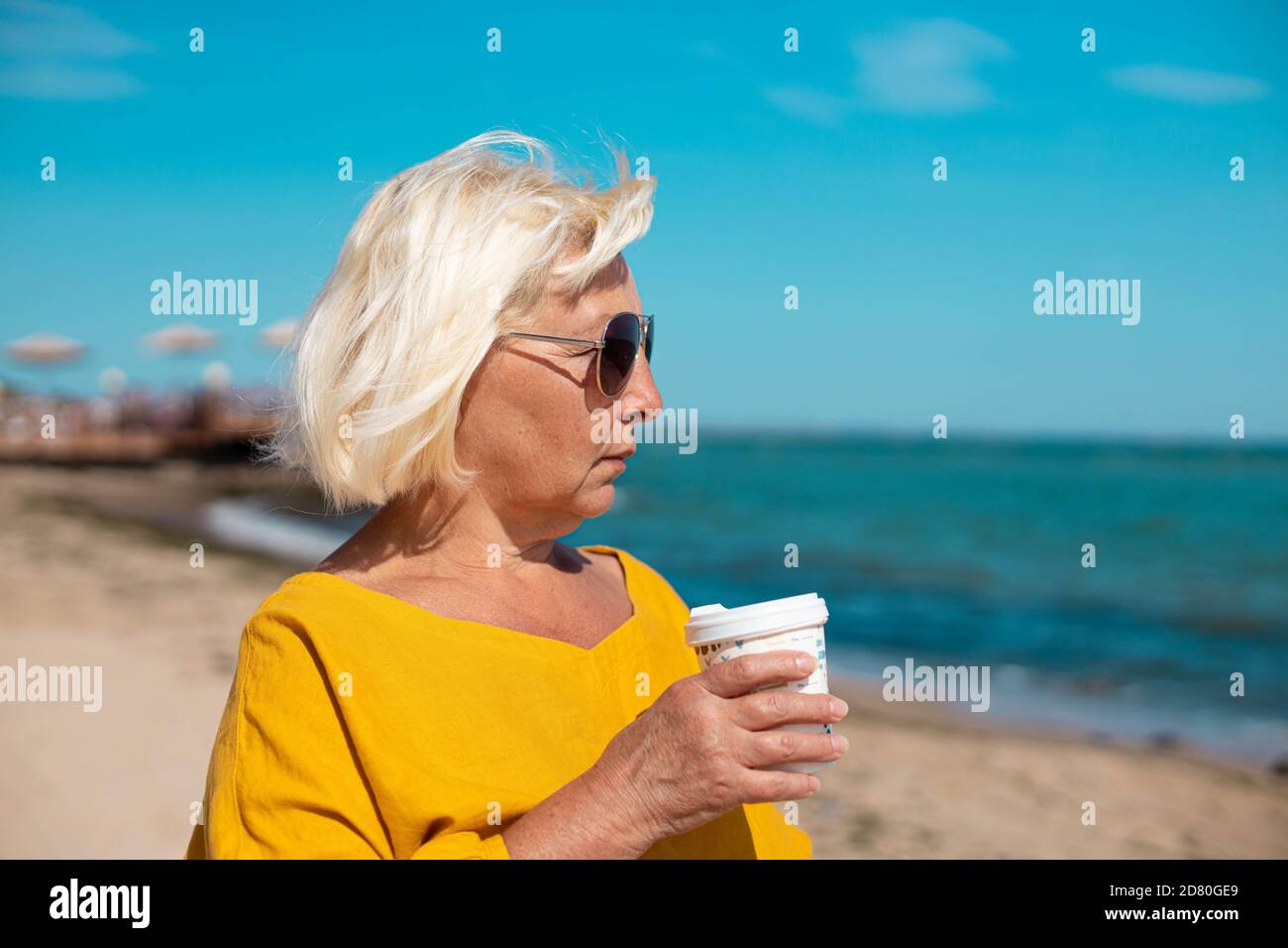 Kaffee zum trinken. Schöne blonde Frau hält Papiertasse Kaffee und genießen einen Spaziergang entlang der Küste Stockfoto