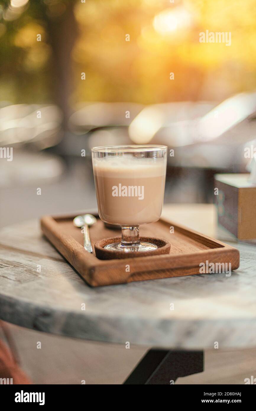 Latte oder Kaffee mit Milchgetränk auf einem Holztablett auf einem Straßentisch im Park. Vertikale Fotoausrichtung Stockfoto