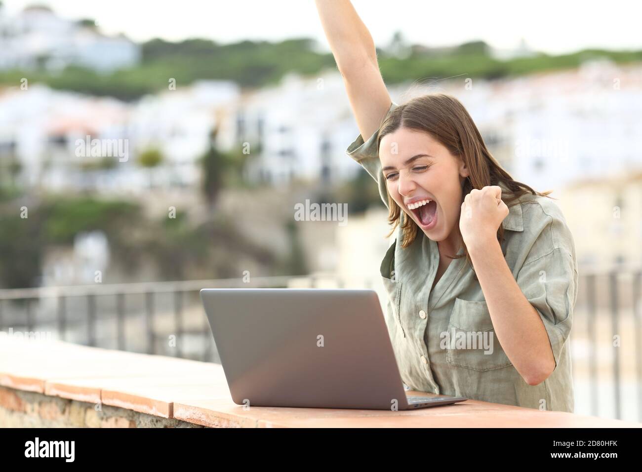 Aufgeregt Frau feiert gute Nachrichten Überprüfung Laptop auf einem Balkon In einer Stadt im Urlaub Stockfoto