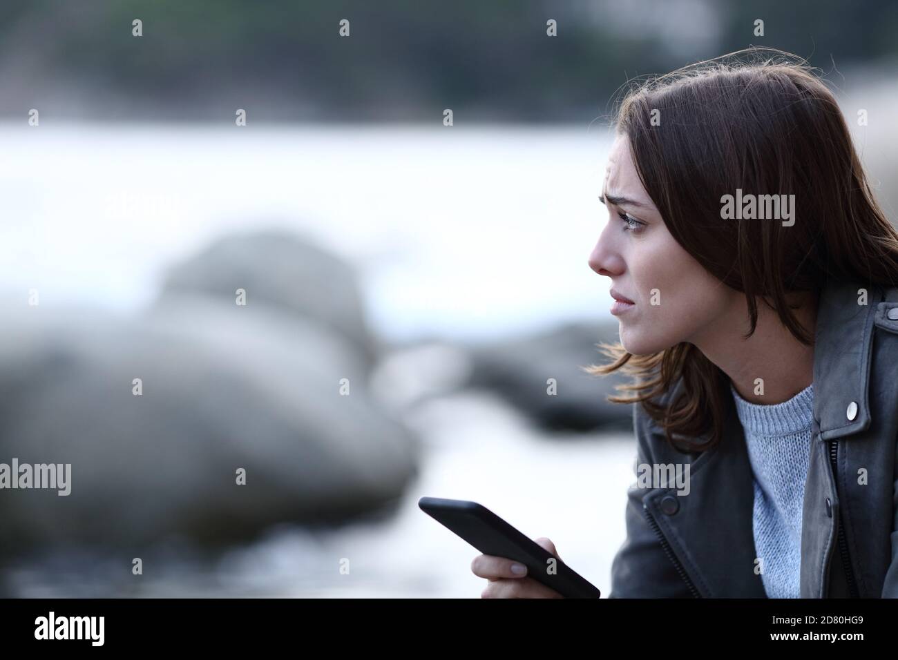 Traurige Frau schaut weg halten Smartphone allein auf dem Strand Stockfoto