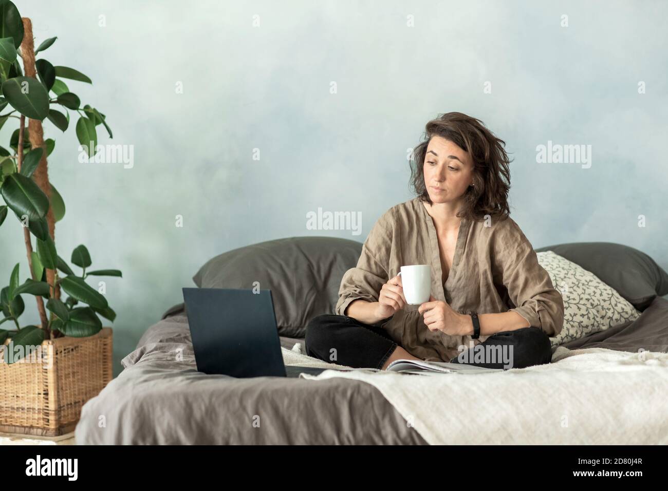 Eine junge Brünette benutzt einen Laptop in ihrem Schlafzimmer, während sie auf dem Sofa sitzt. Stockfoto