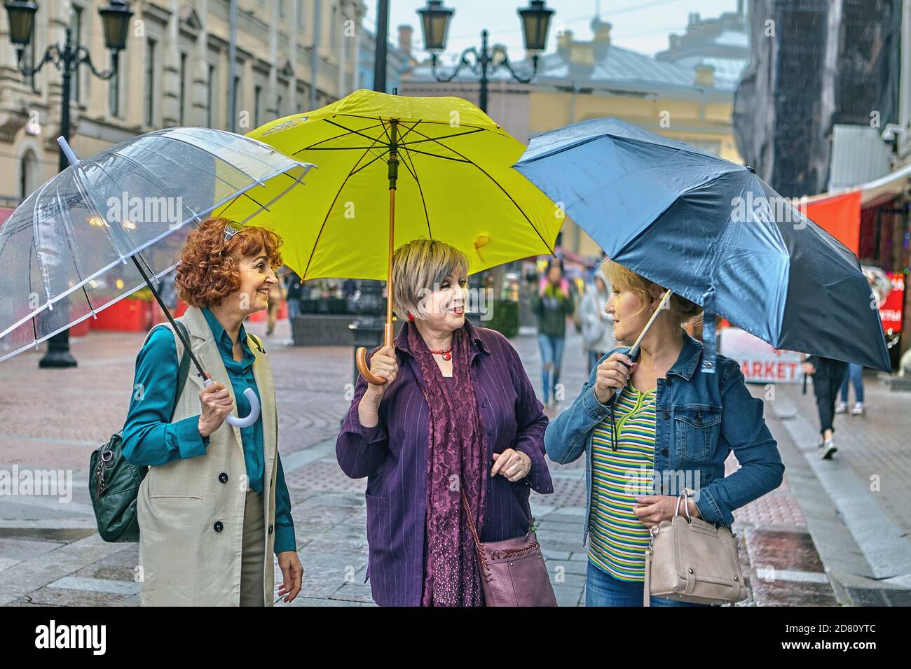 Ältere Frauen mit Sonnenschirmen laufen in der Stadt. Stockfoto