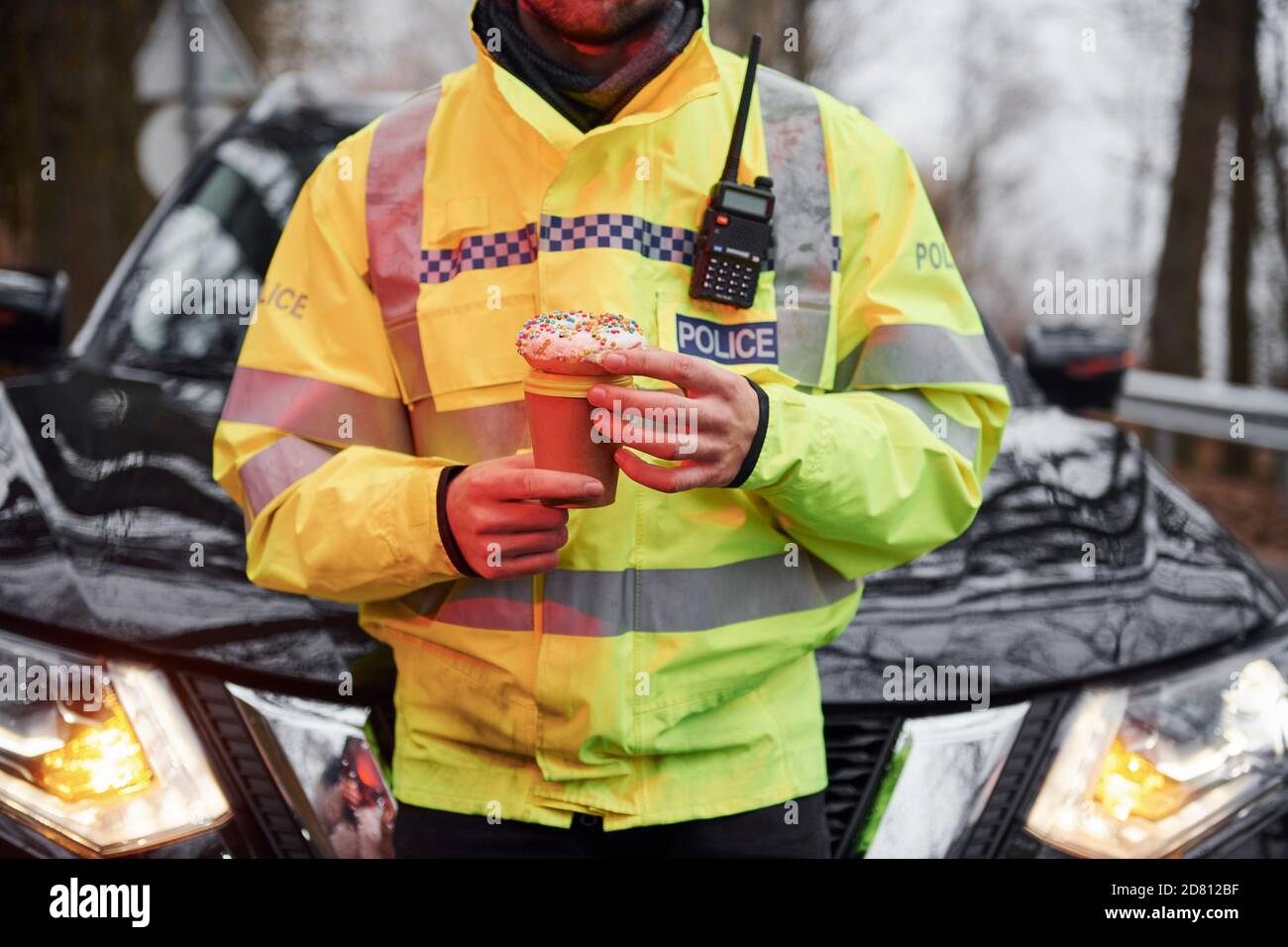 Männlicher Polizist in grüner Uniform, der eine Pause mit nimmt Donut auf der Straße Stockfoto