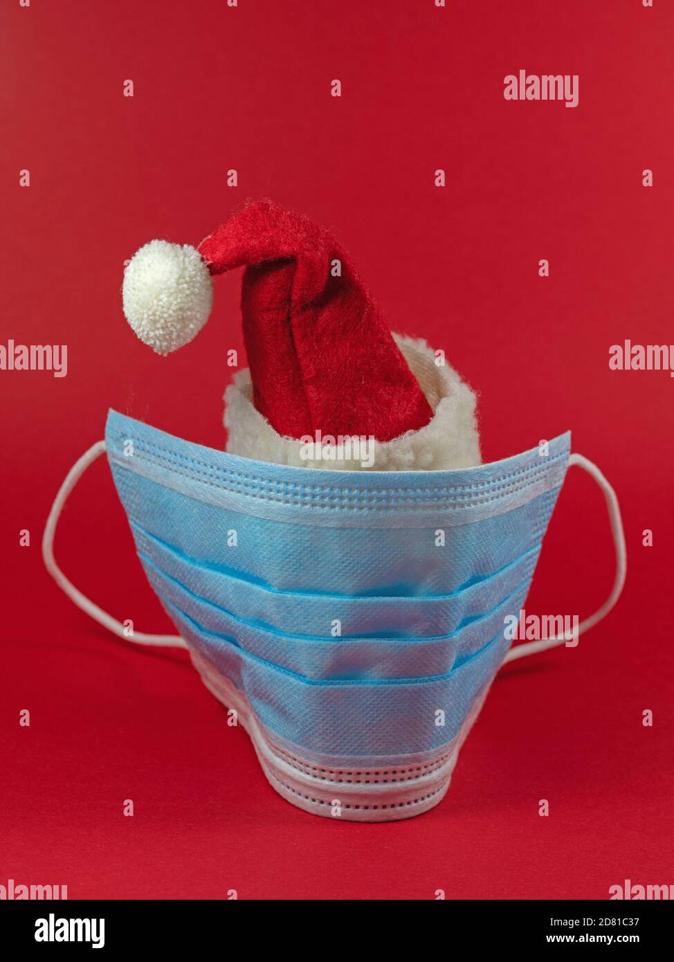 Weihnachtsmann Hut mit Gesichtsmaske vor rotem Hintergrund Stockfoto
