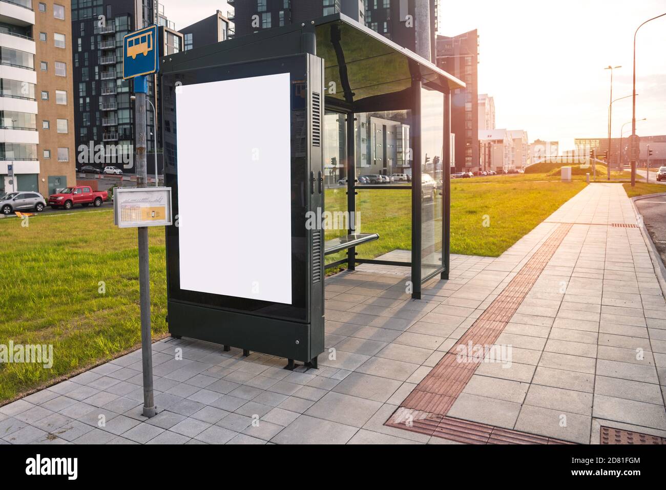 Leere Bushaltestelle mit einem Schutz entlang einer Straße bei Sonnenuntergang. Eine leere Plakatwand befindet sich auf einer der Seiten des Tierheims. Speicherplatz kopieren. Stockfoto