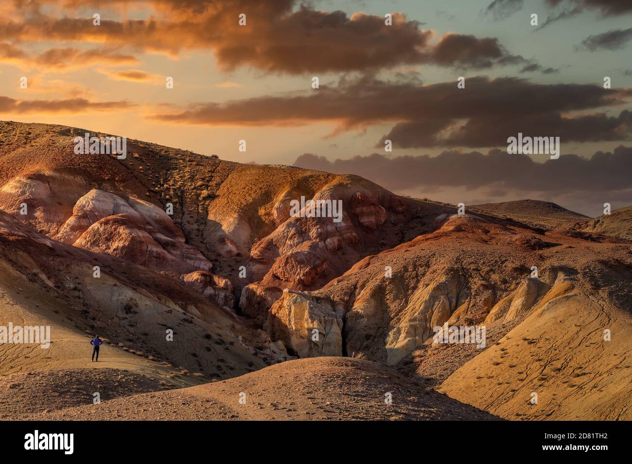 Hochwinkelaufnahme eines Touristen, der vor massiven roten Bergen im Kyzyl-Chin-Tal steht, auch Marstal genannt. Schöner wolkig Sonnenuntergang Himmel wie Stockfoto