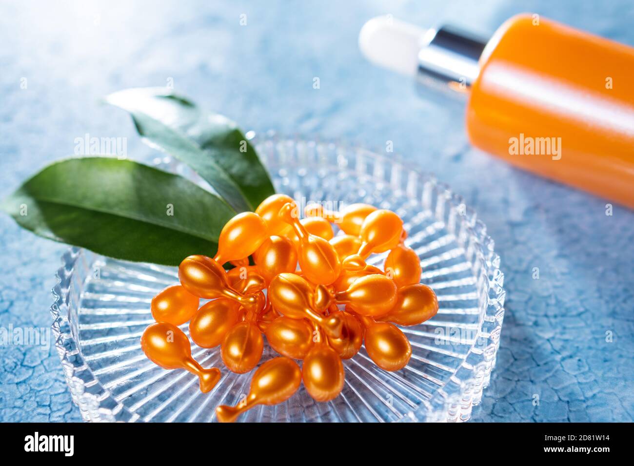 Ein Bündel von Vitamin C Kapseln für die kosmetische Verwendung auf Eine Glasplatte und eine orangene Flasche Serum heraus Der Fokus auf dem Hintergrund auf einem blauen Hintergrund Stockfoto