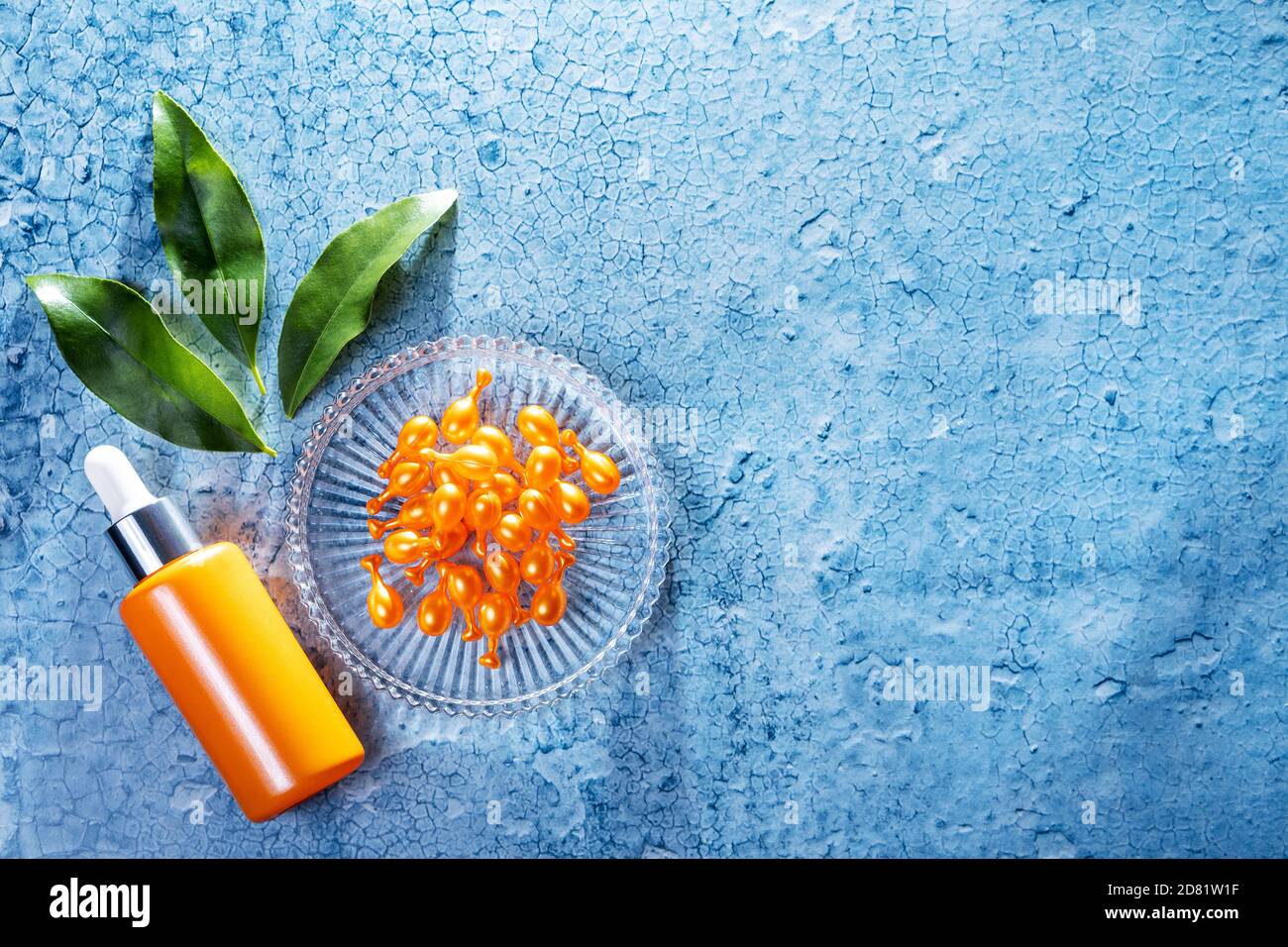 Bunte Komposition von Kosmetikprodukten mit orangen Baumblättern. Eine orangene Flasche Gesichtsserum und viele Vitamin C Konzentrat Kapseln auf einem Glas Stockfoto