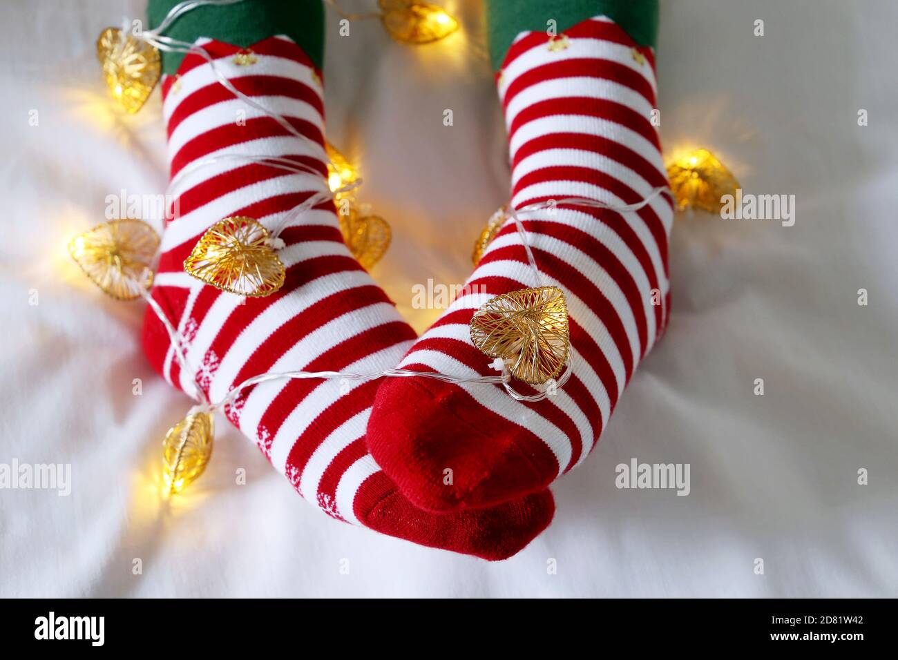 Weibliche Beine in Weihnachtssocken mit Girlande und festlichen Lichtern in Herzform. Konzept der romantischen Silvester Nacht, Elf Kostüm Stockfoto