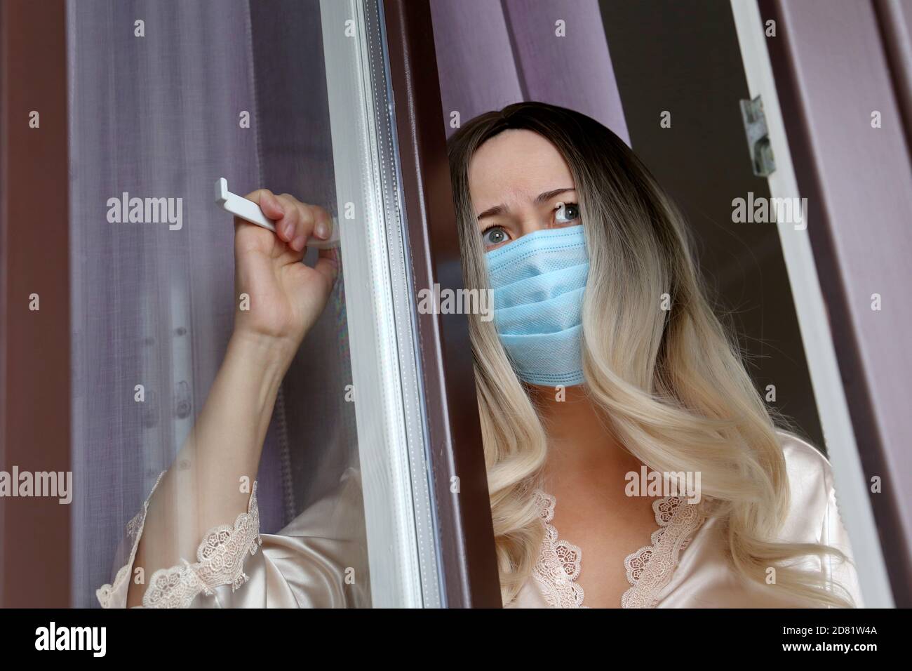Coronavirus-Quarantäne während der covid-19-Epidemie. Besorgt Frau im Gesicht medizinische Maske schaut aus dem Fenster Stockfoto