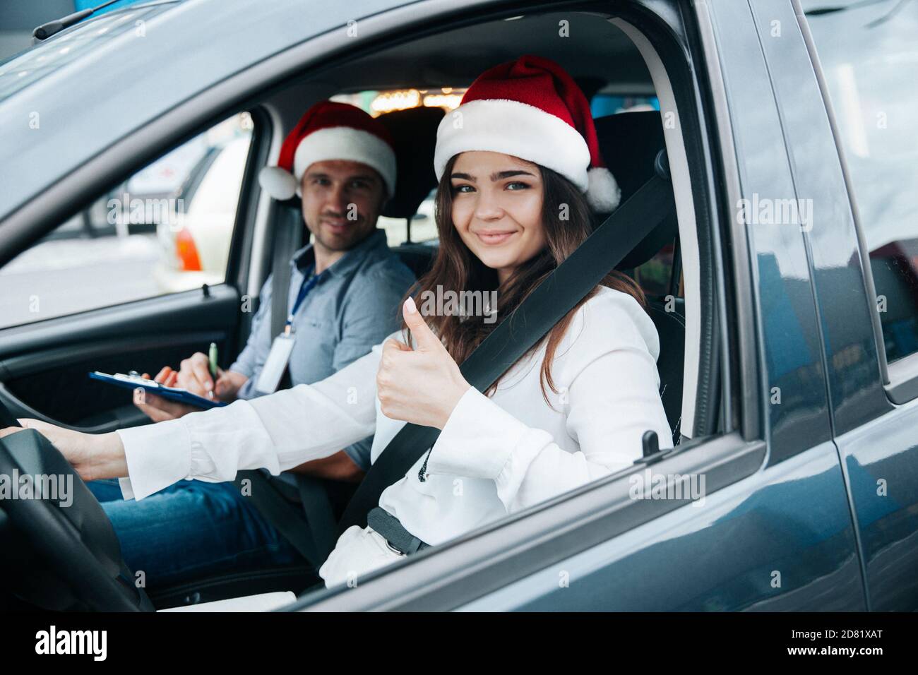 Junge Frau zeigt Daumen nach oben. Frohe Weihnachten und Happy New Year Fahrkurse in den Winterferien. Studentin und Lehrerin in santa Hüte Smili Stockfoto