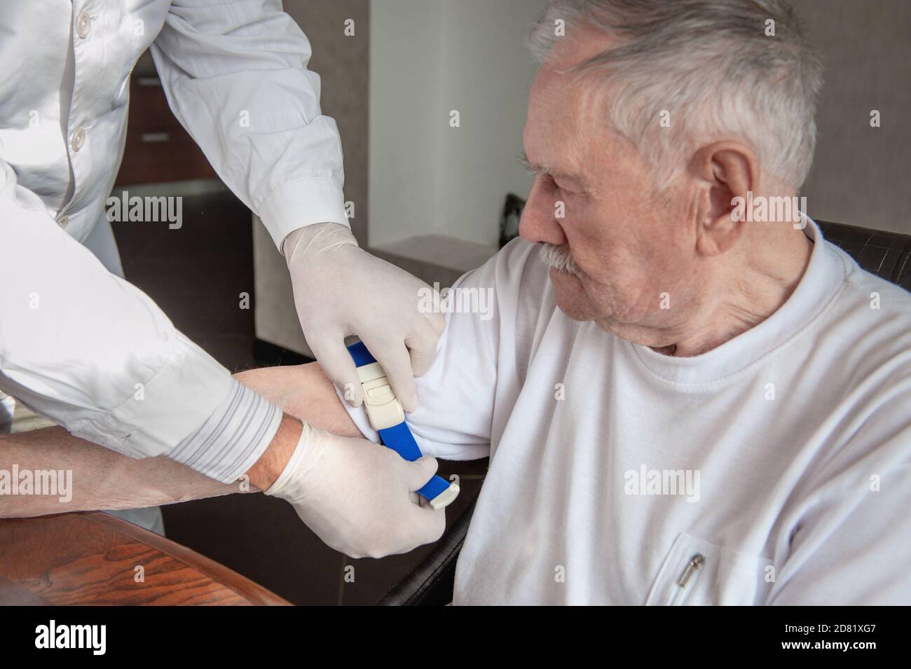 Hände eines Arztes oder eines Arztes sterile Handschuhe, die einen Abbindung auf die Hand eines alten Mannes auftragen. Vorbereitung für die Blutentnahme oder Stockfoto