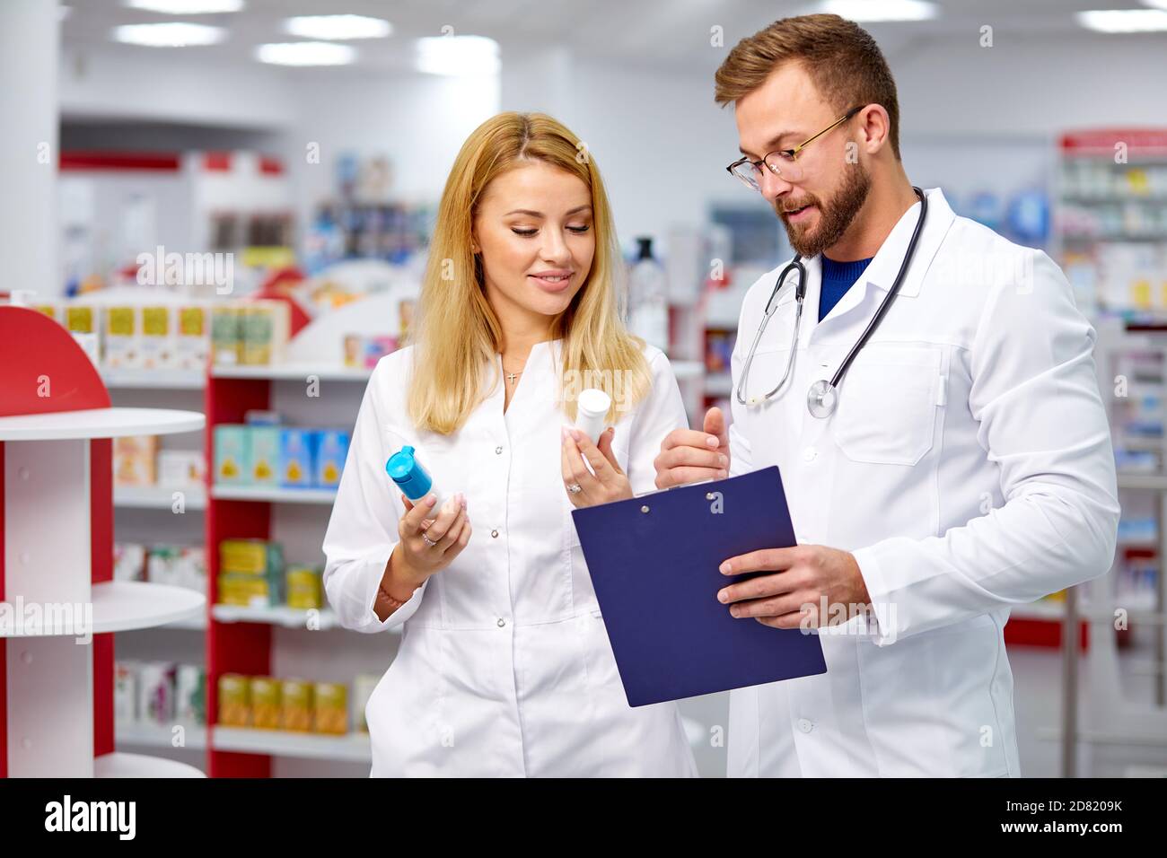 Zwei junge kaukasische Kollegen in weißen medizinischen Kittel Apotheker erfüllen ein Rezept halten Medikamente in der Hand, die Überprüfung der Schrift Stockfoto