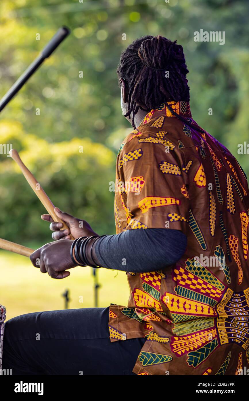 Rückansicht der jungen männlichen Performer mit Dreadlock Haar spielen Trommeln mit Stöcken während des Auftritten auf der Bühne während der Kulturfesta Im Park Stockfoto