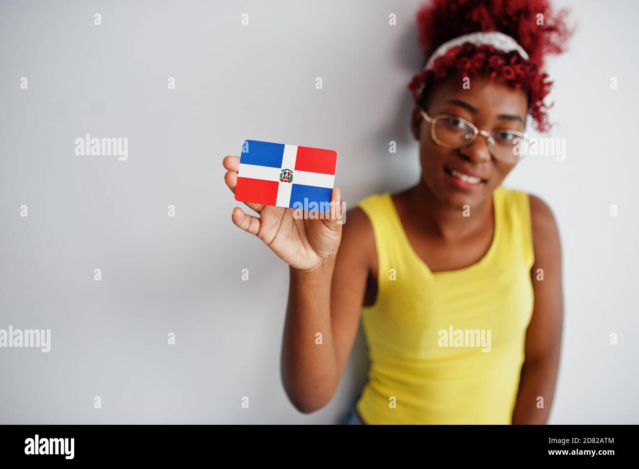 afroamerikanische Frau mit afro Haar, tragen gelbe Singlet und Brillen, halten Dominikanische Republik Flagge isoliert auf weißem Hintergrund. Stockfoto