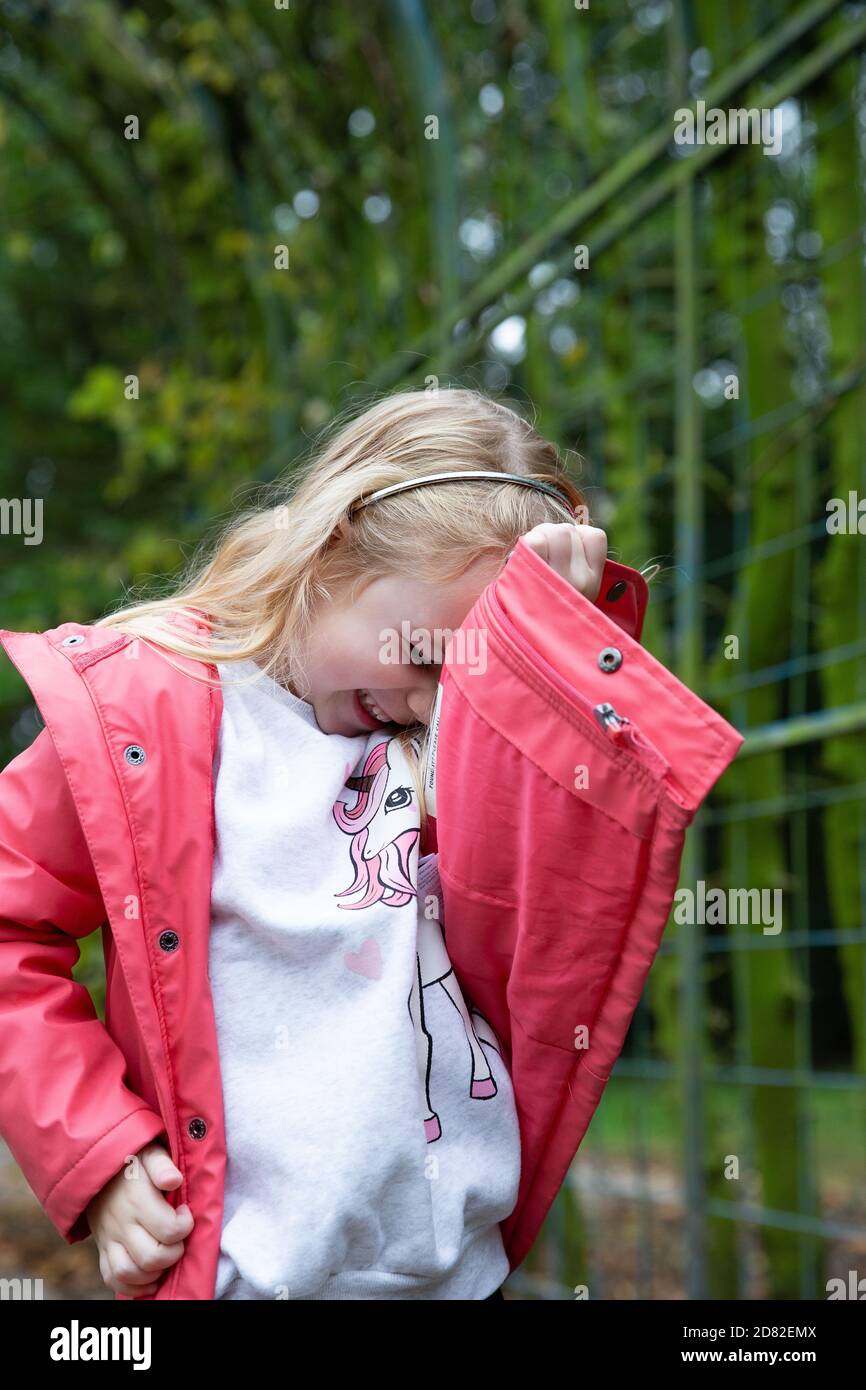 Nettes blondes kleines Mädchen bedeckt ihr Gesicht mit ihrer Hand für das Foto, Privatleben und Kinderkonzept Stockfoto