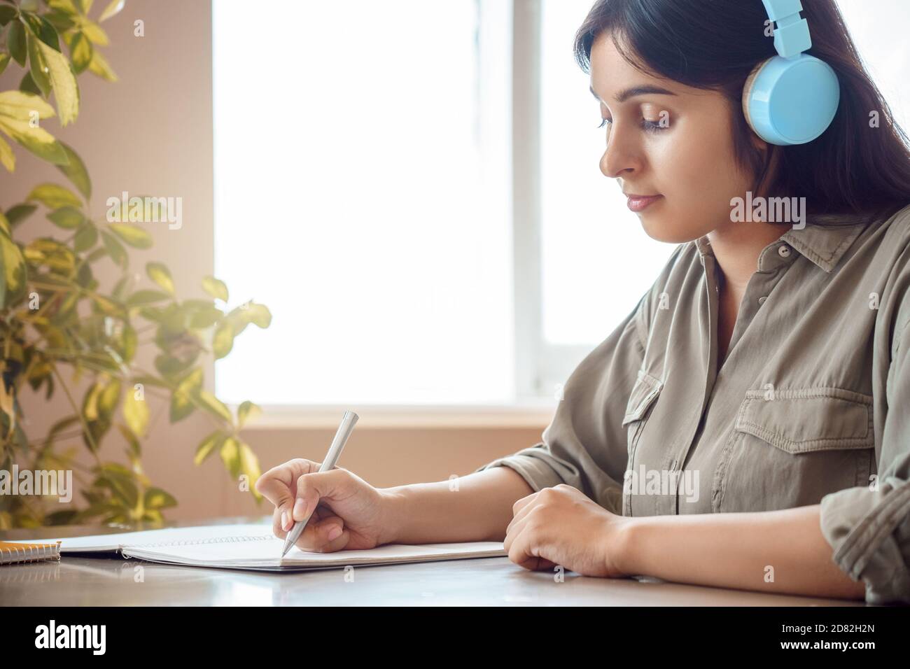 Indische Frau trägt Kopfhörer Schreiben in Notebook Hörkurs zu Hause. Stockfoto