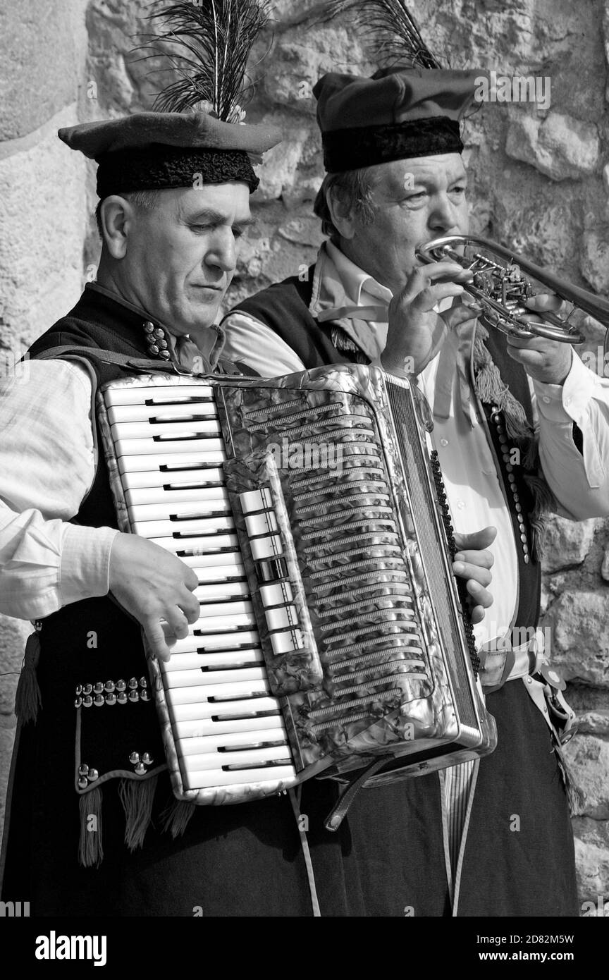 Straßenmusiker spielen Akkordeon und Trompete auf einer Straße in Krakau, Polen. Die beiden Männer sind in traditioneller polnischer Kleidung gekleidet. Stockfoto