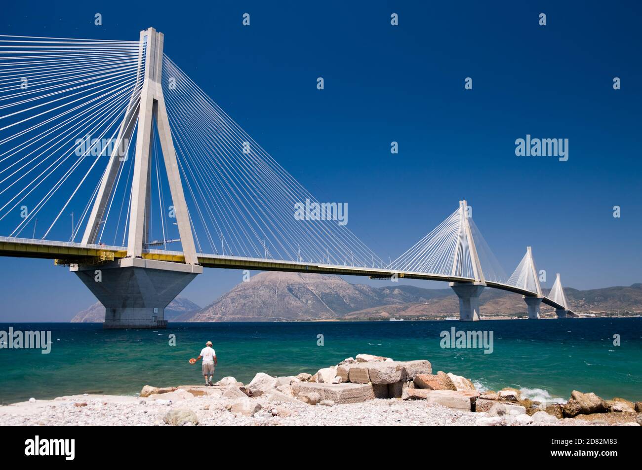 Ein Fischer, der unter der Hängebrücke über die Meerenge des Golfs von Korinth fischt, Griechenland. Stockfoto