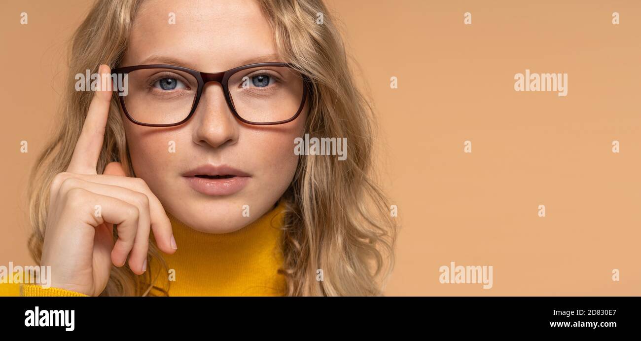 Optische Ladenwerbung, Augenkontrolle. Nahaufnahme Porträt der jungen blonden Frau in Brille Blick auf Kamera isoliert über beige Studio Hintergrund, Stockfoto