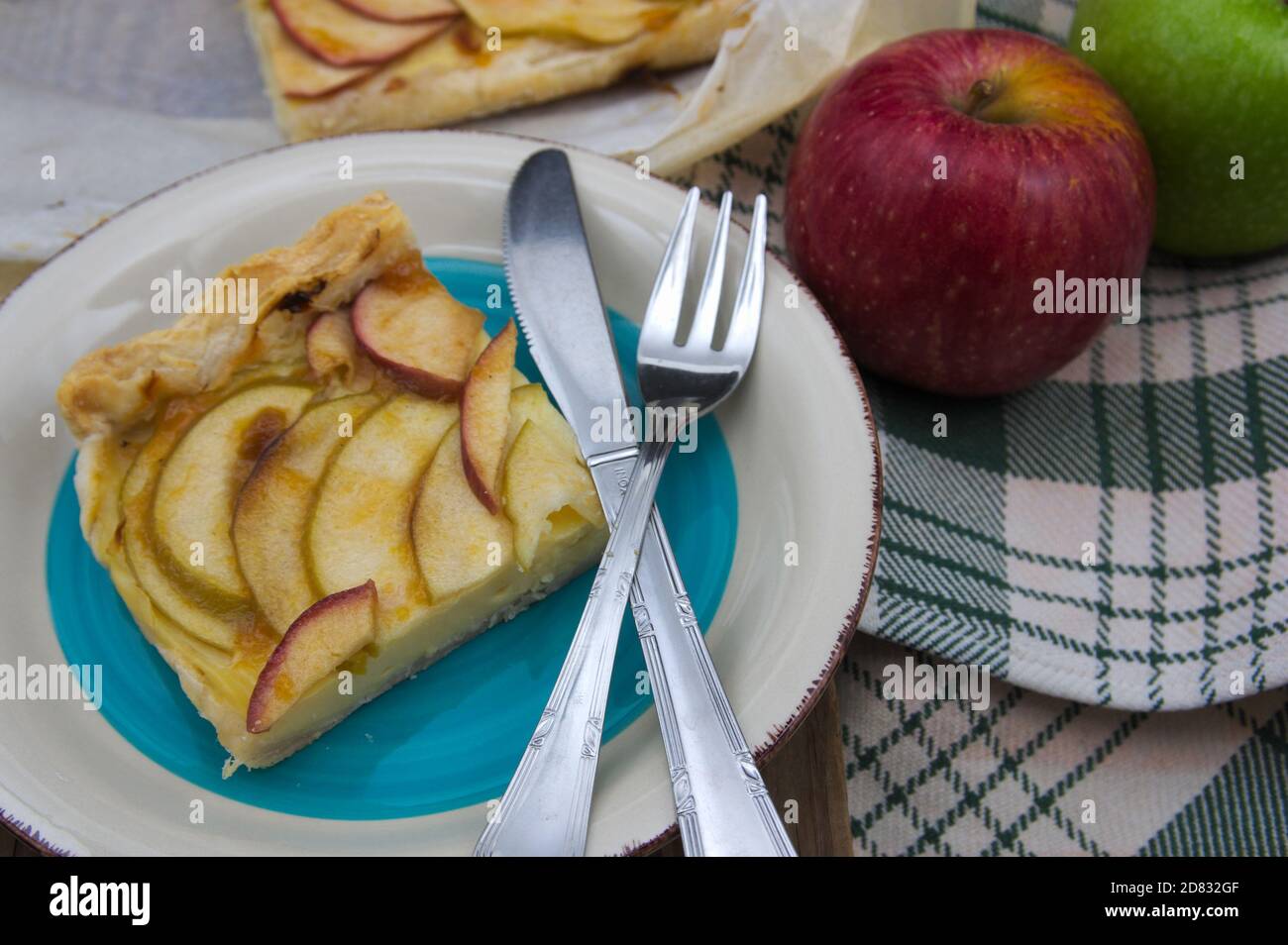 Teller serviert mit einer Scheibe Apfelkuchen mit Pudding neben zwei Äpfeln, einem roten und einem goldenen Stockfoto