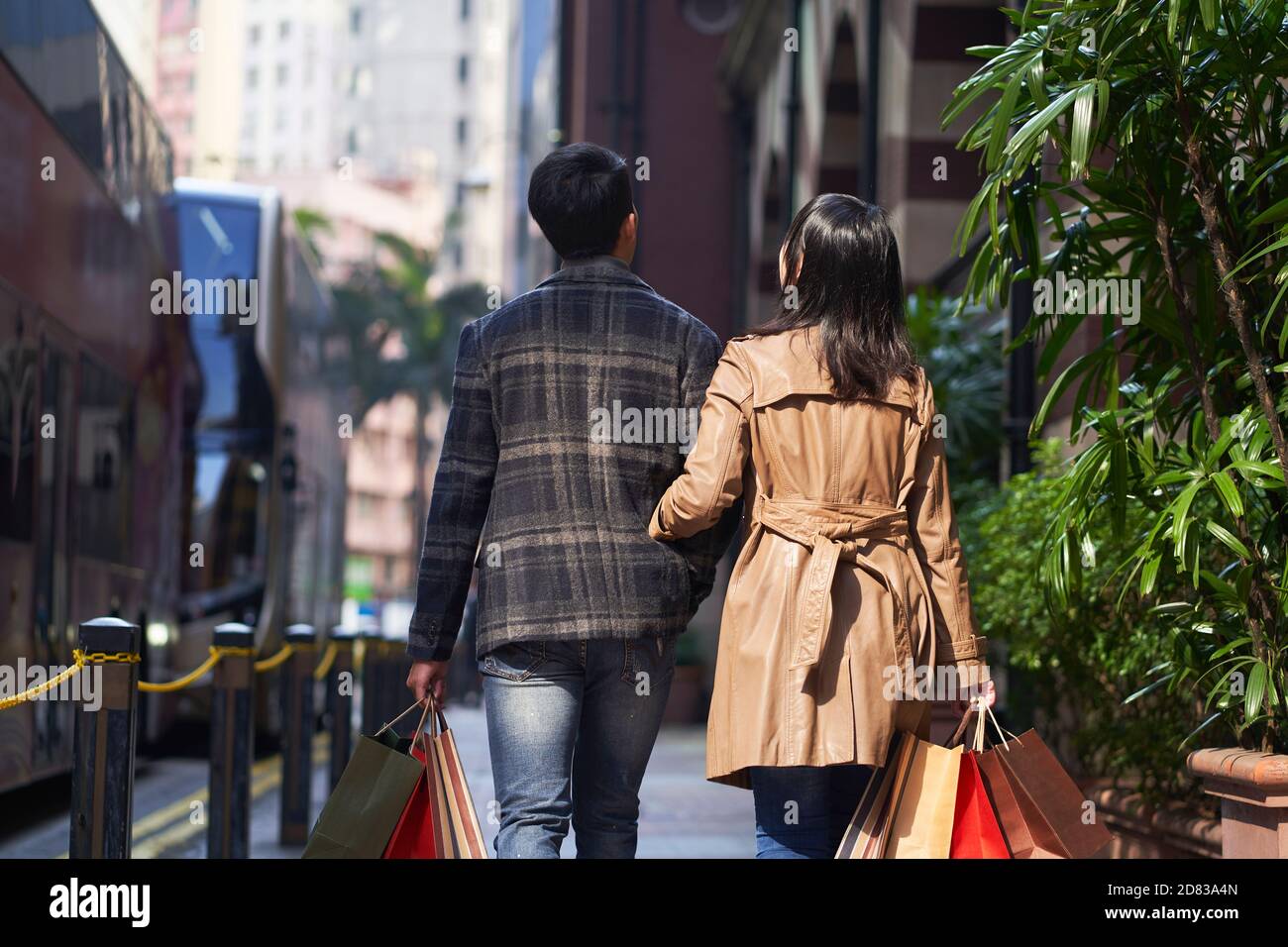 Rückansicht eines jungen asiatischen Paares, das auf der Straße läuft Einkaufstaschen in den Händen Stockfoto