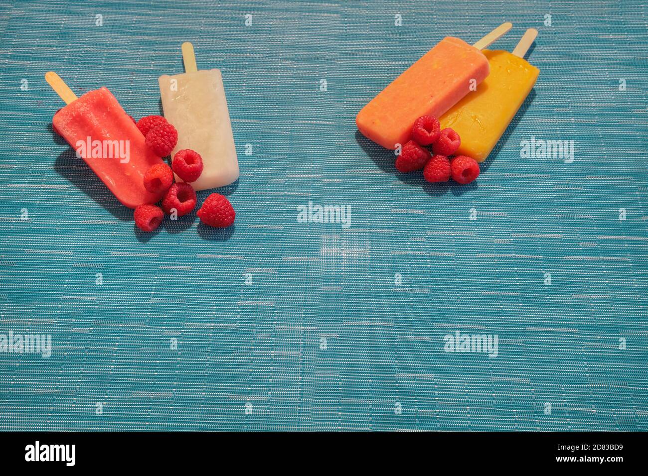 Fruchtpopsicles auf einem aquabluen Hintergrund im Sommer einschließlich Wassermelone Popsicle, tropische Frucht Popsicle, Mango Popsicle, und Limettenpopsicle mit Fr. Stockfoto