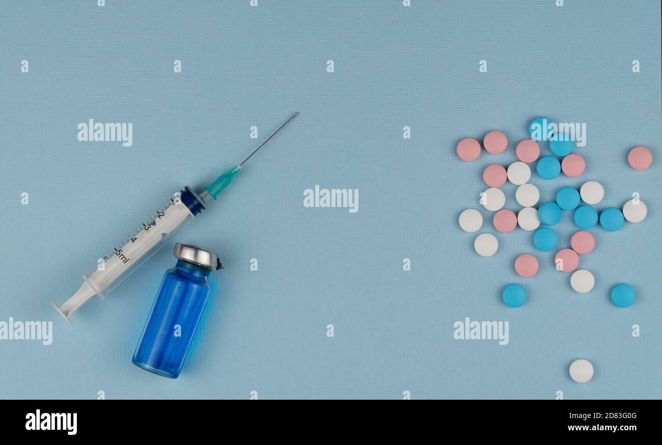 Medizinische Spritze und bunte Pillen auf blauem Hintergrund. Wählen Sie zwischen Impfung und Behandlung Stockfoto